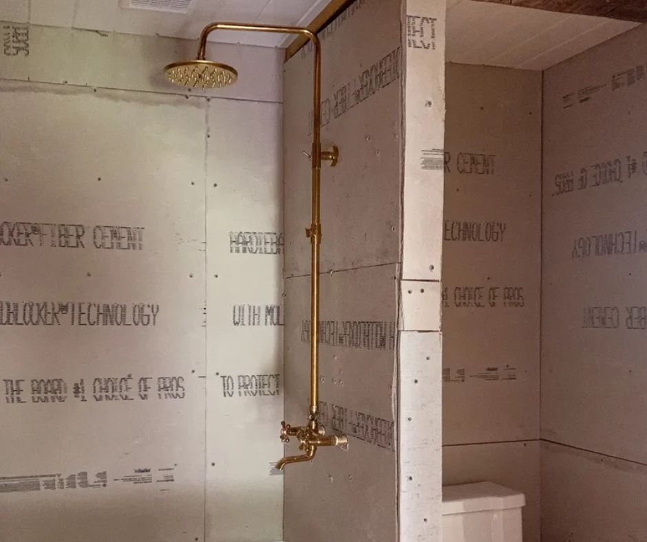 Gold shower fixture on unfinished wall.